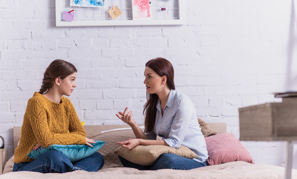Junge Mutter und Tochter sitzen auf dem Bett und diskutieren.