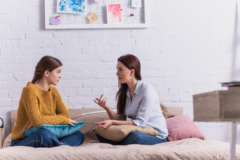 Junge Mutter und Tochter sitzen auf dem Bett und diskutieren.