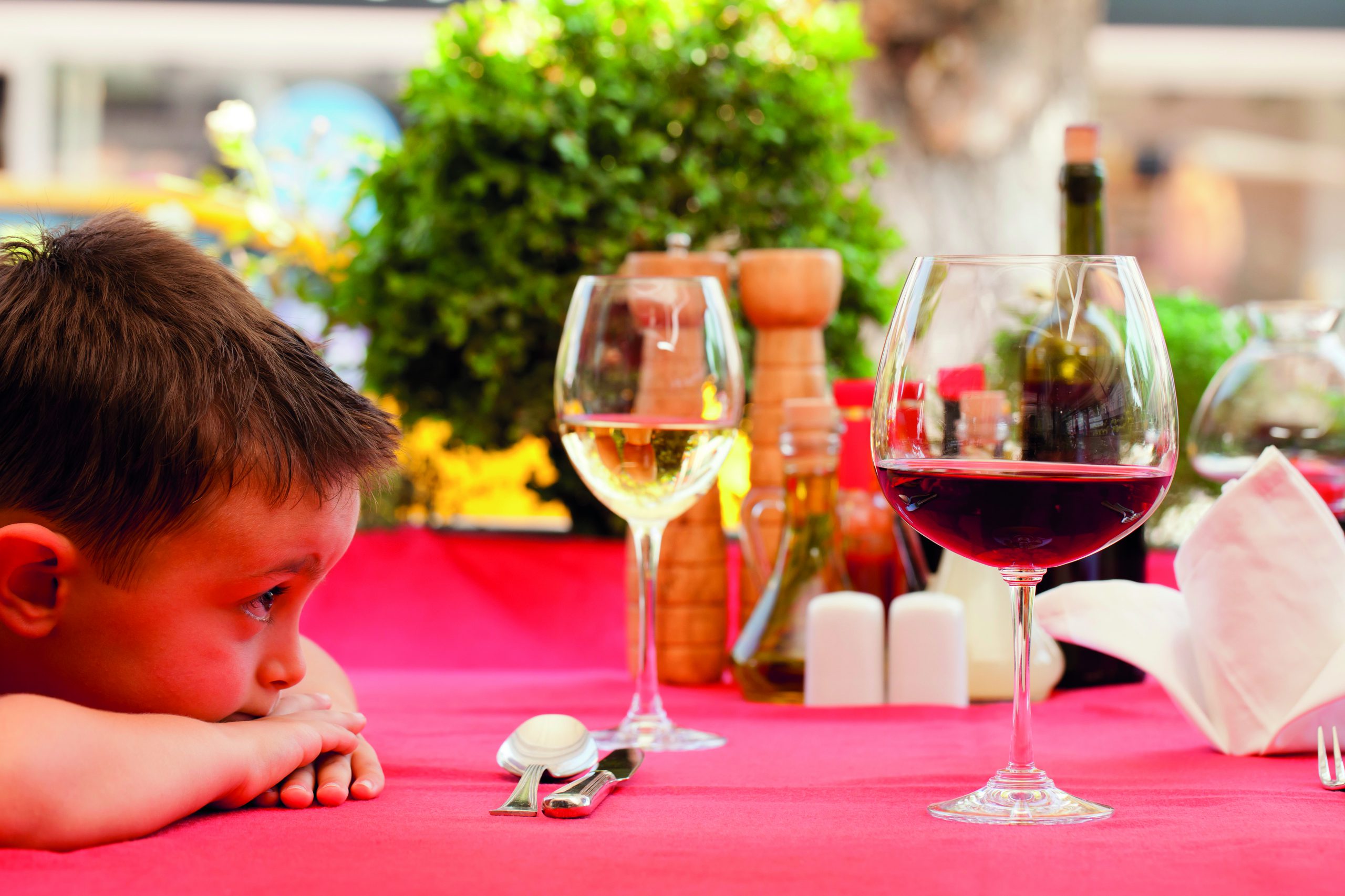 Kind schaut interessiert auf eine volles Weinglas.