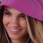 Nahaufnahme eines lächelnden Mädchens im Regen mit Kopfhörern in den Ohren und einem lila Regenmantel