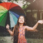 junge Frau mit Regenschirm allen Farben des Regenbogens im Regen